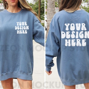 Könnte beinhalten: Ein blaues Oversize-Sweatshirt mit dem Text "YOUR DESIGN HERE" in Weiß auf Vorder- und Rückseite. Der Text ist in einer Retro-Schriftart mit Blasenform.