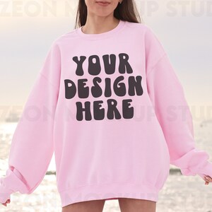 May include: A pink sweatshirt with the text "YOUR DESIGN HERE" in black, bubble letters.