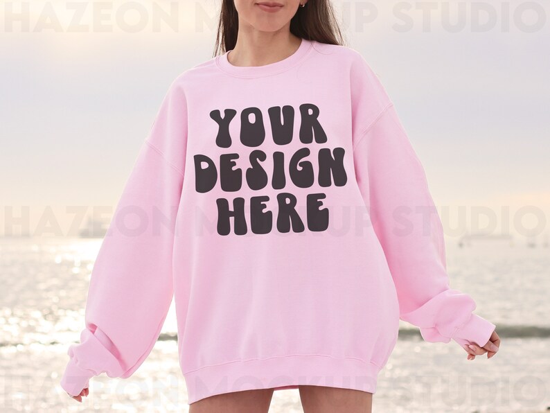 May include: A pink sweatshirt with the text "YOUR DESIGN HERE" in black, bubble letters.