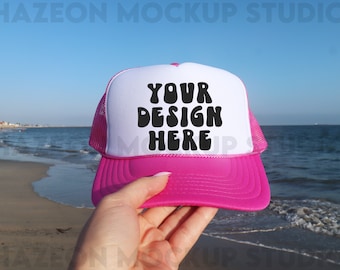 Op de afbeelding: Roze en witte truckercap met een wit voorpaneel en een roze mesh achterkant. Het voorpaneel heeft de tekst "YOUR DESIGN HERE" in zwart.