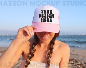 Op de afbeelding: Een roze en witte truckercap met een zwart mesh achterpaneel. De pet heeft de tekst "YOUR DESIGN HERE" in zwarte blokletters op de voorkant.