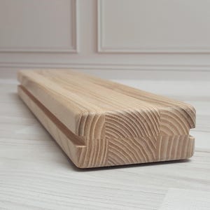 Può includere: Un oggetto rettangolare in legno chiaro con un design scanalato. La venatura del legno è visibile e l'oggetto sembra essere composto da diversi blocchi uniti. Potrebbe essere un tagliere o un vassoio da portata.
