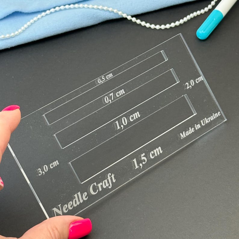 K&ouml;nnte beinhalten: Eine transparente, rechteckige Acryl-Schablone f&uuml;r Handarbeiten mit vier rechteckigen Aussparungen, die mit 0,5 cm, 0,7 cm, 1,0 cm und 1,5 cm beschriftet sind. Das Werkzeug enth&auml;lt die eingravierten Texte Needle Craft, 3,0 cm, 2,0 cm und Made in Ukraine.