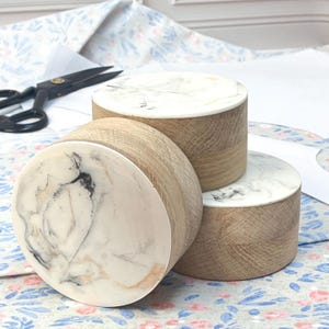 Könnte beinhalten: Drei runde Holzkuchenständer mit weißen Marmorplatten. Die Ständer sind übereinander gestapelt, wobei der größte unten und der kleinste oben ist.