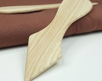 May include: A wooden tool with a pointed tip and a curved handle. The tool is made of light-colored wood with a natural grain pattern.