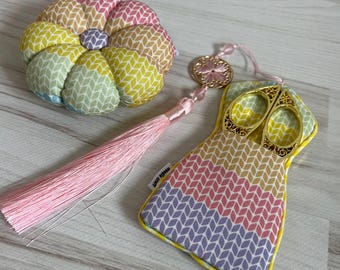May include: A set of colorful sewing tools with a rainbow patterned pincushion, a pair of gold scissors, and a pink tassel.