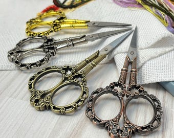 May include: Four pairs of decorative scissors with ornate floral designs. The scissors are in gold, silver, and copper tones.