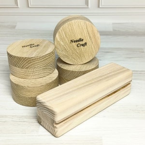 Può includere: Set di quattro basi rotonde in legno e un blocco rettangolare in legno con una scanalatura. Le basi sono impilate l'una sull'altra e il blocco è sdraiato sul lato. Le basi sono tutte in legno chiaro e hanno le parole "Needle Craft" incise.