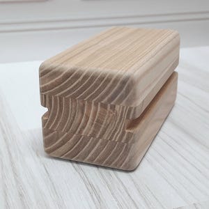 May include: A wooden block with a natural finish and a groove cut into the top. The block is made of two pieces of wood that are stacked on top of each other.