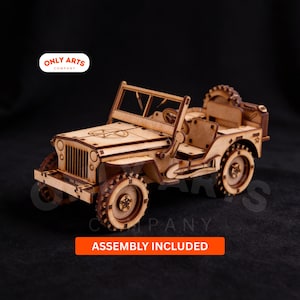 Può includere: Modello in legno di una jeep d'epoca, con dettagli intagliati al laser. Il modello è di colore marrone chiaro e include una ruota di scorta, un volante e un'emblema a stella. Il testo "ASSEMBLY INCLUDED" è visualizzato su un banner arancione.