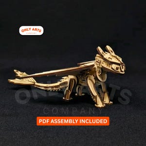Puede incluir: Modelo de dragón de madera con alas extendidas y detalles. El modelo es de madera clara y está ensamblado. La imagen incluye el texto "PDF ASSEMBLY INCLUDED" en un recuadro rojo y el logotipo "ONLY ARTS COMPANY".