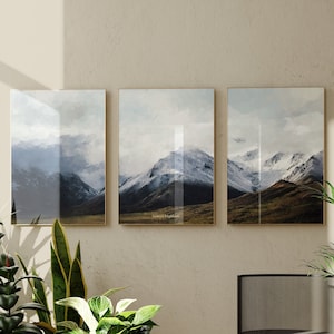 Może przedstawiać: Trzy oprawione zdjęcia krajobrazowe ze śnieżnymi szczytami gór i zielonym, trawiastym pierwszym planem. Zdjęcia wiszą na beżowej ścianie, na pierwszym planie znajduje się czarne krzesło i zielone rośliny.