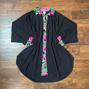 May include: Black long-sleeve shirt with a floral and animal print design on the collar, cuffs, and front. The shirt has a rounded hemline and a button-up front. The floral print includes pink and green flowers.