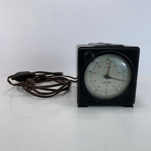 May include: A vintage black electric timer with a round clock face. The face has white numbers and a red second hand. The timer is labeled "Standard" and has a brown power cord.