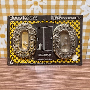 May include: Vintage Deco Room recessed sliding door pulls. The pulls are oval-shaped with a decorative border and a brass finish. The packaging includes the text "Easy to Install" and "Rustproof Dura-Metal."