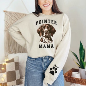 May include: A beige sweatshirt with the text "POINTER MAMA" in black letters and a brown and white German Shorthaired Pointer dog illustration. The sweatshirt has a black paw print on the left sleeve with the word "Name" above it.