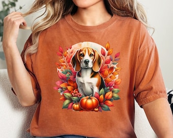 May include: A brown t-shirt with a graphic of a beagle dog sitting in a circle of autumn leaves and pumpkins. The dog is brown and white with a black nose and brown eyes.