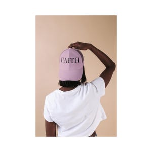 Peut inclure: Une casquette de type trucker violet clair avec un arrière en filet et le mot FAITH imprimé en lettres capitales noires sur le panneau avant. La casquette présente une calotte structurée et une visière courbée, portée avec un t-shirt blanc.