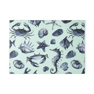 May include: A rectangular mat featuring a repeating watercolor pattern of dark blue sea creatures and shells on a light mint green background. The design includes crabs, starfish, a seahorse, various spiral seashells, and small fish illustrations.