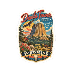 May include: A die-cut sticker featuring Devils Tower National Monument in Wyoming. The illustration shows a hiker with a backpack, a flying eagle, a bison, and a buffalo skull. Text reads: Devils Tower National Monument, Where Earth Touches Sky, WYOMING.