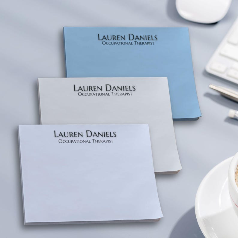 May include: Three stacks of personalised notepads with the name "Lauren Daniels, Occupational Therapist" printed on each. The notepads are in blue, white, and light blue.