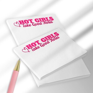 May include: White sticky note pads with the text "HOT GIRLS Take Good Notes" in pink. A pink pen with a gold tip is in the foreground. The pads are stacked on top of each other.