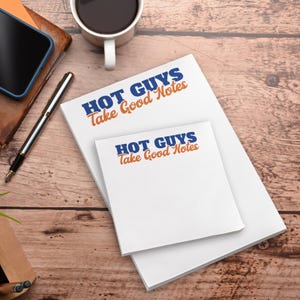 May include: White notepads with the text "HOT GUYS Take Good Notes" in blue and orange. A pen, a smartphone, and a cup of coffee are on a wooden surface.