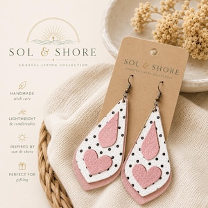 May include: Leather teardrop earrings with a pink heart and polka dot design. The earrings are layered with white and pink leather. The earrings are on a brown card with the text "SOL & SHORE COASTAL LIVING COLLECTION".