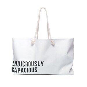 Könnte beinhalten: Weiße Tragetasche mit Seilgriffen und dem schwarzen Aufdruck "LUDICROUSLY CAPACIOUS". Die Tasche ist rechteckig und scheint aus einem glatten Material zu bestehen. Die Griffe sind hellbeige.
