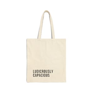 Könnte beinhalten: Eine cremefarbene Tragetasche mit dem dunkelbraunen Aufdruck "LUDICROUSLY CAPACIOUS". Die Tasche hat zwei Henkel und besteht aus einem robusten Stoff, ideal zum Tragen von Lebensmitteln, Büchern oder anderen Gegenständen.