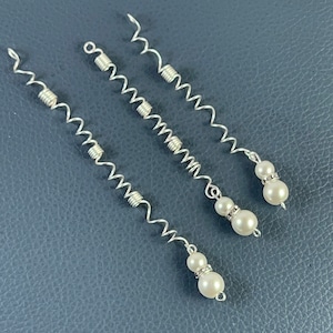May include: Three silver hair clips with pearl accents. Each clip has a wavy, spring-like design.