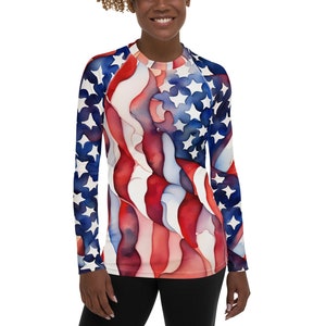 May include: A long-sleeved shirt with a watercolor design of the American flag. The shirt is white with red and blue stripes and white stars.
