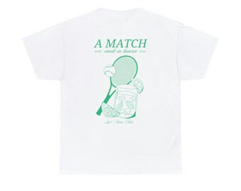 Op de afbeelding: Wit T-shirt met een groene afbeelding van een tennisracket, een tennisbal, een glas limonade en de tekst "A MATCH made in heaven". De tekst "Last Name Here" is ook opgenomen in de afbeelding.
