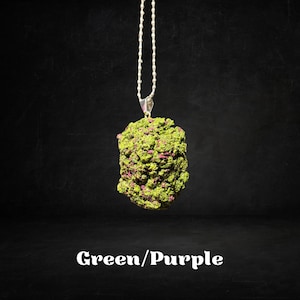 May include: A silver chain necklace with a green and purple pendant shaped like a bud. The pendant is textured and has a rough surface.