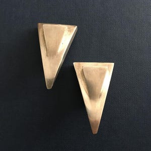 May include: A pair of silver triangle shaped earrings. The earrings are geometric and modern in style.