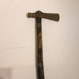 May include: A vintage hatchet with a wooden handle and a metal head. The handle is dark brown with silver bands. The hatchet head is a rusty brown color. The hatchet is a tool.