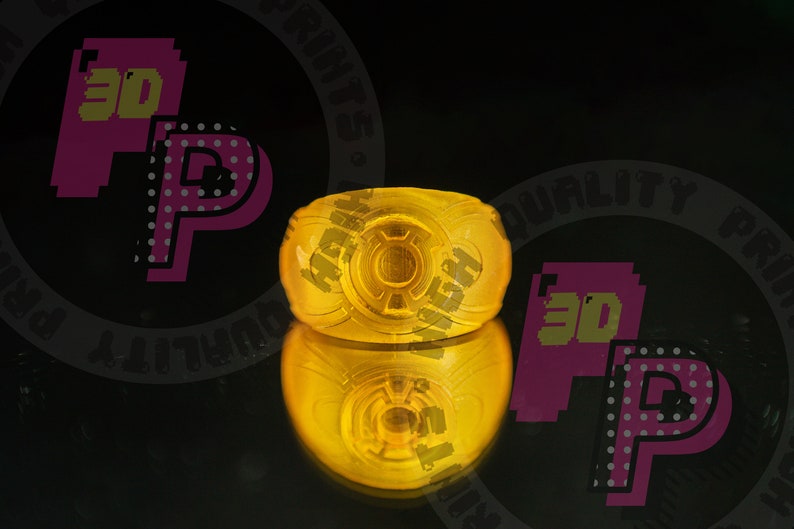 Pu&ograve; includere: Un anello giallo traslucido con un emblema circolare sulla parte anteriore. Il design include un motivo circolare centrale circondato da un bordo rialzato, creando un distinto motivo in rilievo. Il materiale appare liscio e lucido.
