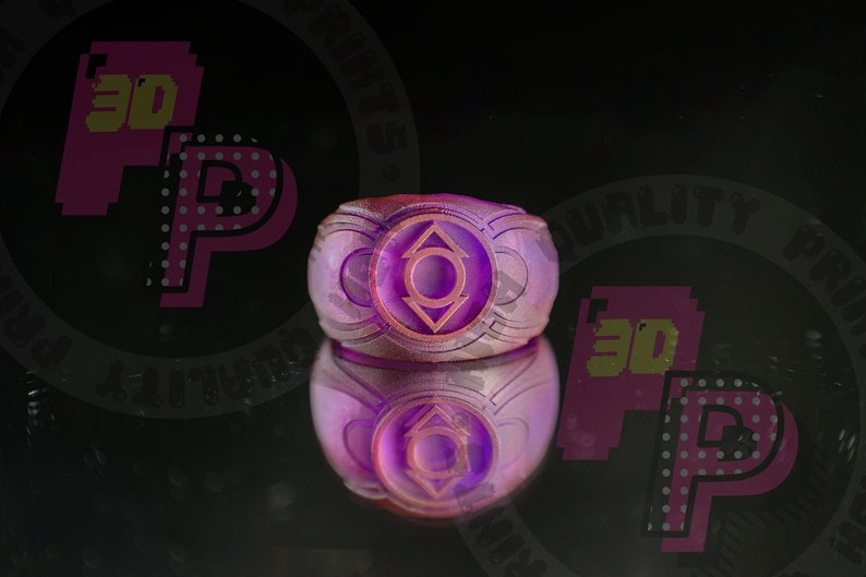 Pu&ograve; includere: Un anello viola con un emblema circolare caratterizzato da un cerchio centrale e due triangoli rivolti verso l'alto e verso il basso. L'anello presenta una finitura superficiale testurizzata e stratificata su uno sfondo scuro.