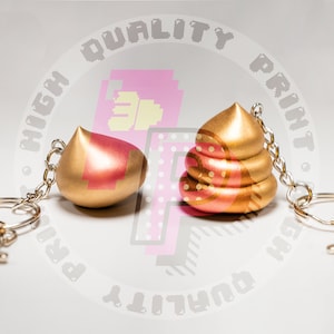 May include: Two gold-colored keychains with different shaped charms. One charm is a simple rounded shape, the other is a three-dimensional poop shape.