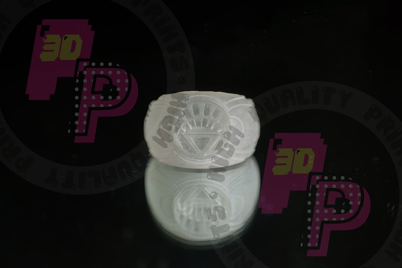 Pu&ograve; includere: Un anello bianco traslucido caratterizzato da un emblema circolare in rilievo con un triangolo centrale e linee radianti. L'anello presenta una finitura liscia e opaca e un design a fascia larga con un simbolo grafico chiaramente impresso.