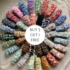 Puede incluir: Colección de coleteros coloridos con varios estampados, incluyendo cuadros, flores y colores lisos. Los coleteros están dispuestos en forma circular con el texto "BUY 3 GET 1 FREE" en el centro. Los coleteros son de tela.
