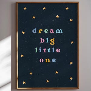 May include: A framed print with a dark blue background and gold stars. The text "dream big little one" is written in colorful letters.