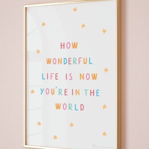May include: A white framed print with the text "How Wonderful Life Is Now You're In The World" in colourful letters. The print is decorated with small yellow stars.