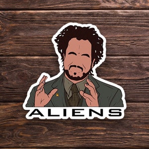 May include: A sticker featuring a cartoon illustration of a man with curly hair and a beard, wearing a suit and tie. The man is making a gesture with his hands, and the text "ALIENS" is below him.