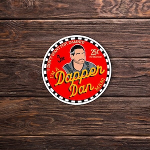 May include: A red and white circular sticker with the text "I'm a Dapper Dan" and "I don't want fop. Damnit!"  The sticker also features a cartoon illustration of a man with a mustache and a 3 oz. label.