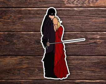 Op de afbeelding: Een sticker met een zwart geklede figuur met een masker die een zwaard vasthoudt, naast een vrouw in een rode jurk.