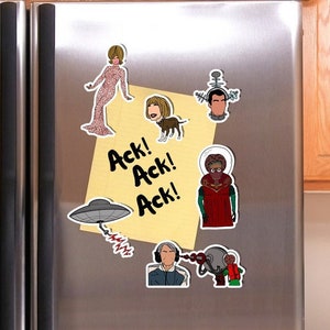 May include: A set of refrigerator magnets featuring characters from the popular TV show "The Jetsons". The magnets include a woman in a pink dress, a man with a large head, a dog, a flying saucer, and a robot. The magnets are yellow, red, blue, and black.