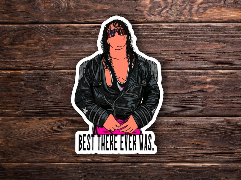 May include: A black and white illustration of a wrestler wearing a black leather jacket, sunglasses, and a pink and black wrestling outfit. The text "BEST THERE EVER WAS." is below the image.