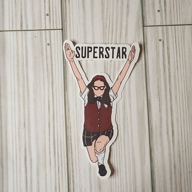 Puede incluir: Una pegatina con una ilustraci&oacute;n de dibujos animados de una persona con uniforme escolar con los brazos levantados, sosteniendo una pancarta que dice "SUPERSTAR". La persona lleva gafas, una diadema roja y un chaleco granate.