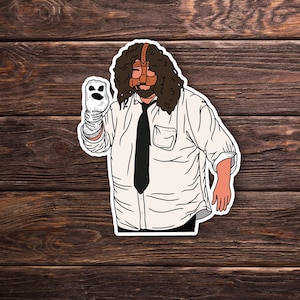 May include: A sticker of a person with long brown hair wearing a white shirt, a black tie, and a brown leather mask. The person is holding a white puppet with a smiling face.